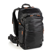 An image of the Shimoda Explore V2 25 Backpack Starter Kit Black. The backpack is black with rust coloured zips and has a carry handle, pockets for water bottles or tripods and multiple zipped pockets with shoulder straps and a removeable belt.