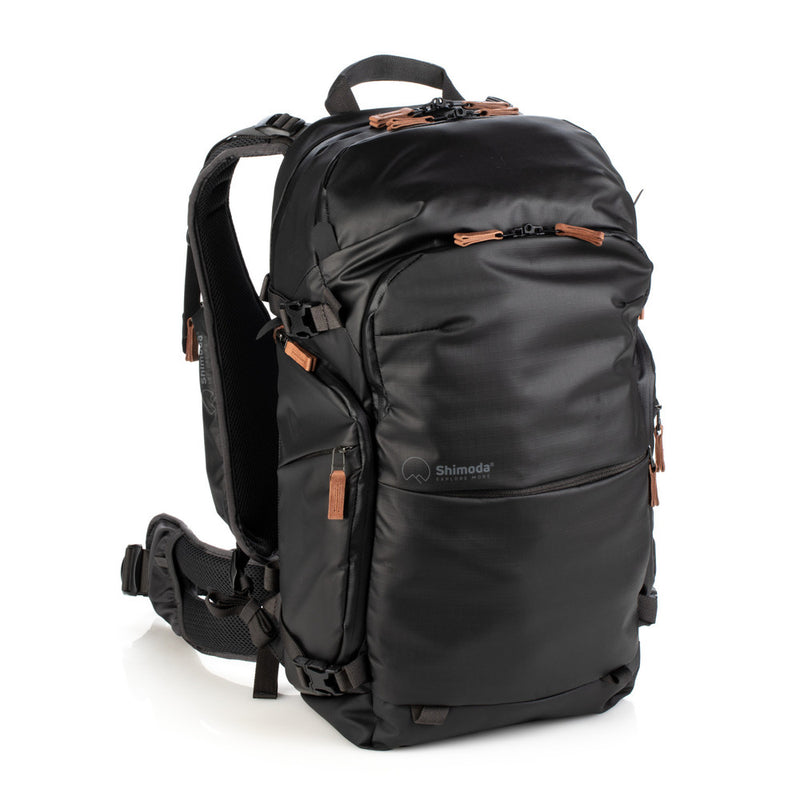 An image of the Shimoda Explore V2 25 Backpack Starter Kit Black. The backpack is black with rust coloured zips and has a carry handle, pockets for water bottles or tripods and multiple zipped pockets with shoulder straps and a removeable belt.