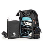 An image of the Shimoda Explore V2 25 Backpack Starter Kit Black with the back compartment open. The backpack is black with rust coloured zips and has a carry handle, pockets for water bottles or tripods and multiple zipped pockets with shoulder straps and a removeable belt. Inside the backpack is a laptop, water bottle, camera and other photographic equipment.