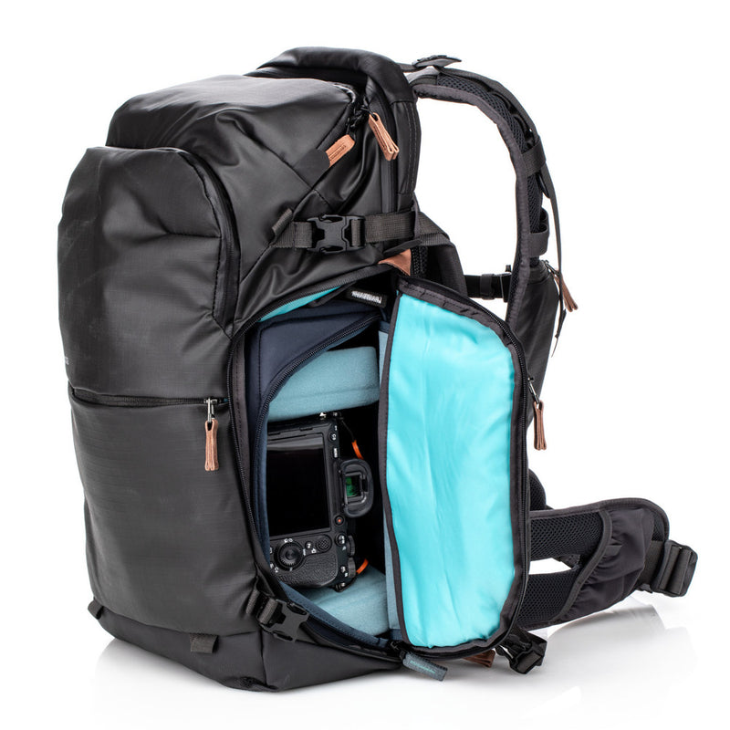 An image of the Shimoda Explore V2 25 Backpack Starter Kit Black with the side compartment open showing a DSLR camera stored. The backpack is black with rust coloured zips and has a carry handle, pockets for water bottles or tripods and multiple zipped pockets with shoulder straps and a removeable belt.